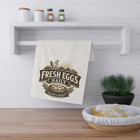 Kitchen towel with 'Fresh Eggs Daily' design hanging on a shelf above a wooden counter with a basket of bread.